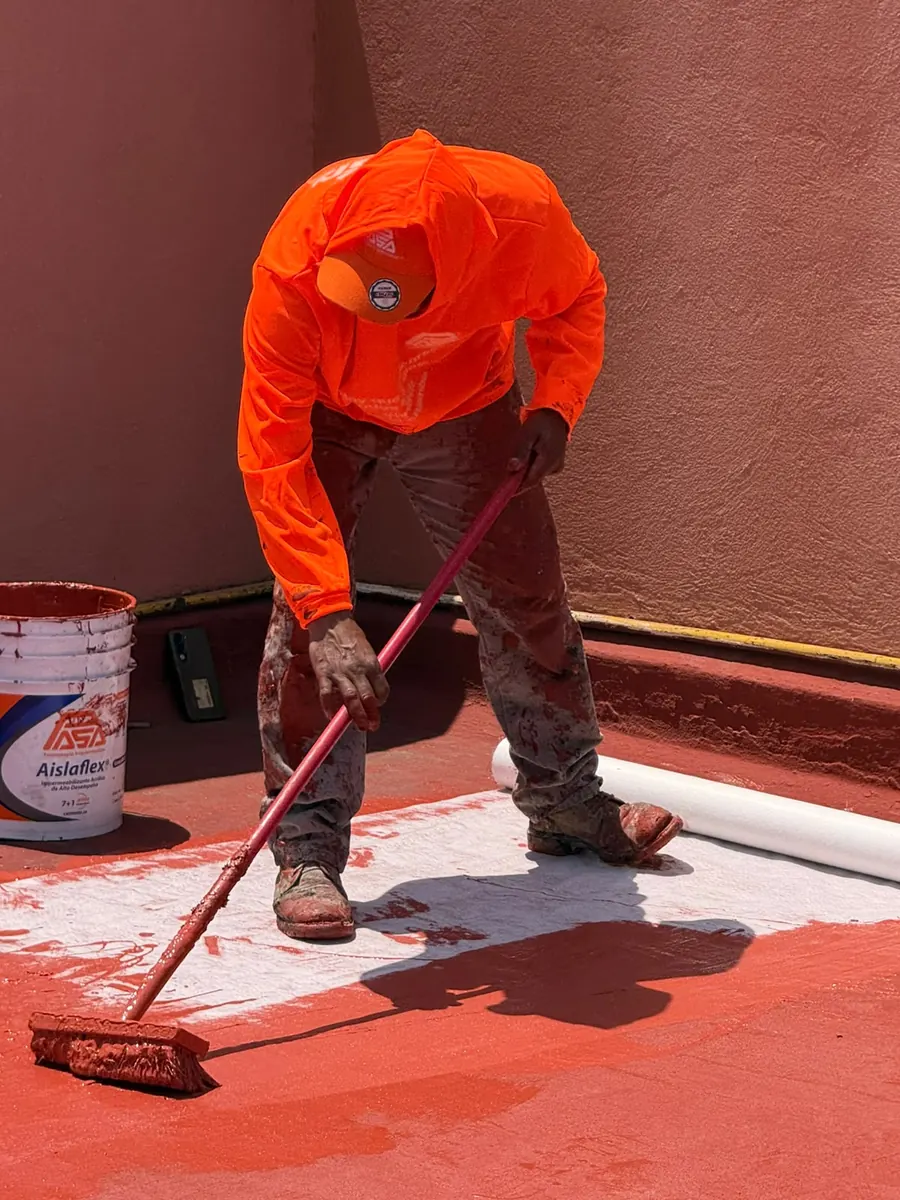 Aplicador colocando impermeabilizante acrílico rojo sobre malla de refuerzo