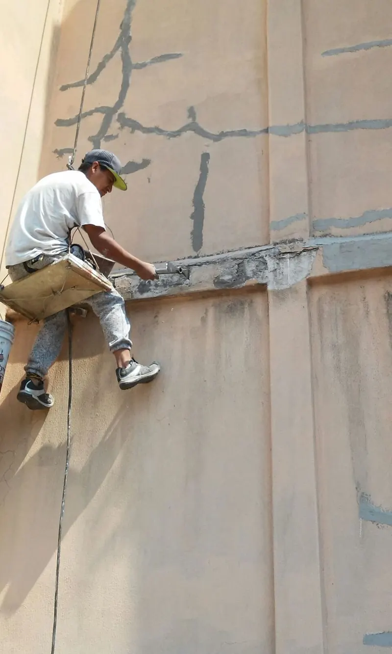 Técnico en rapel sellando grietas en un muro alto